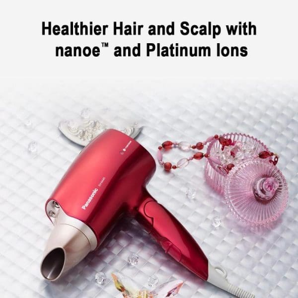 Red Panasonic EH-NA45 Nanoe hair dryer with nozzle attachment on white textured surface, surrounded by decorative pink glass items and jewelry accessories.
