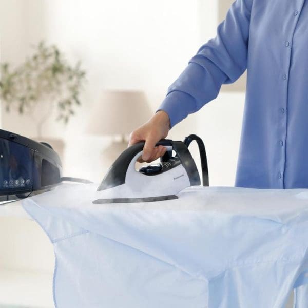 Person in blue shirt using Panasonic NI-GT150ASK steam generator iron to press white fabric on ironing board in bright, clean home setting.