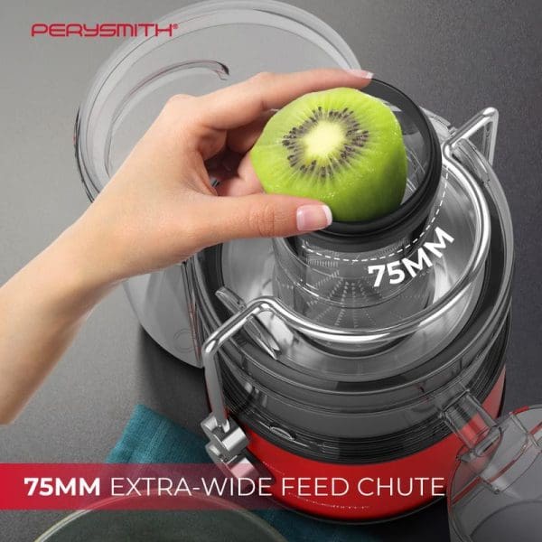 PerySmith J2000 juice extractor with 75mm extra-wide feed chute, hand placing kiwi fruit into the transparent juicing chamber, red and clear plastic construction.