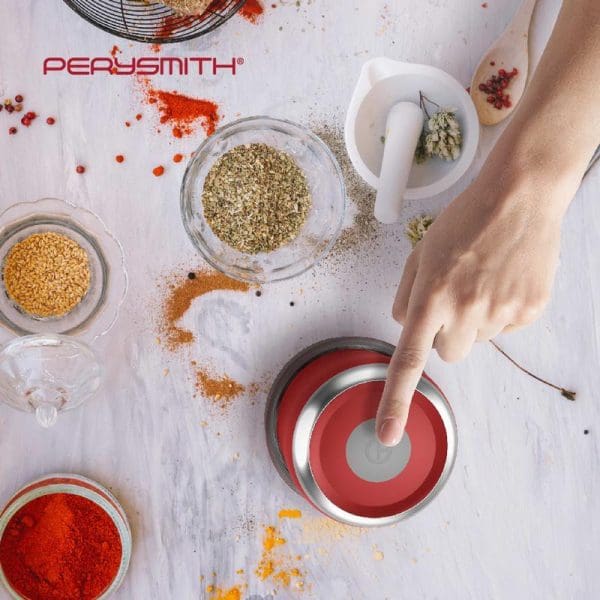 PerySmith Mini Food Chopper PS250 in red with various spices and herbs scattered around, showing hands using the cordless kitchen appliance for food preparation.