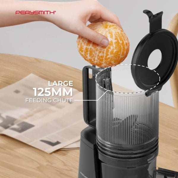PerySmith PS600 slow juicer with large 125mm feeding chute, hand placing peeled orange into the wide opening, showcasing easy fruit juicing capability.
