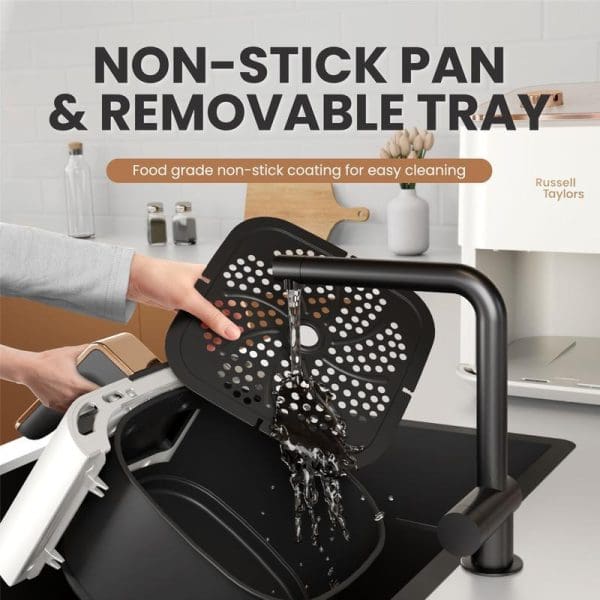 Russell Taylors air fryer with removable non-stick perforated tray being washed under kitchen sink faucet, demonstrating easy cleaning feature in modern white kitchen.