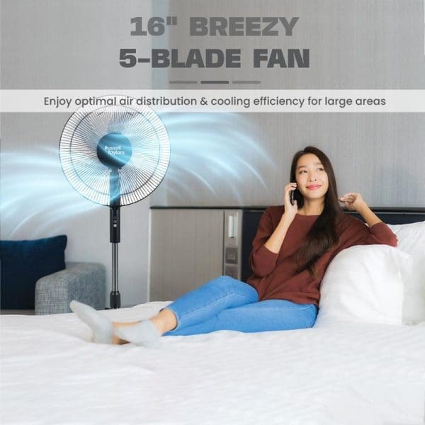 Russell Taylors 16-inch Breezy 5-blade stand fan providing optimal air distribution and cooling efficiency, shown with woman relaxing on bed while talking on phone.