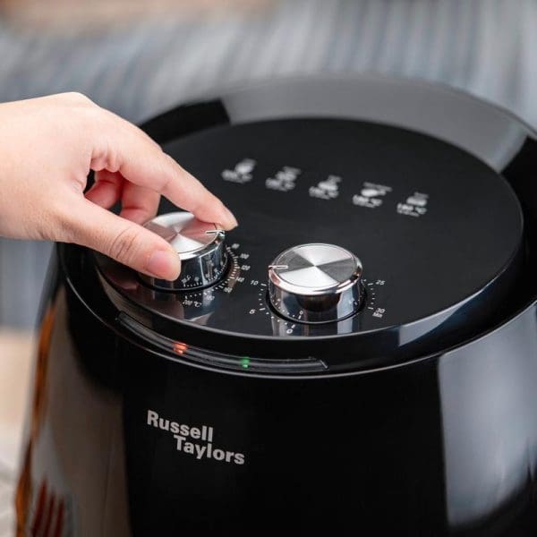 Hand adjusting temperature dial on black Russell Taylors AF-34 XL 4.8L Air Fryer with digital display and control knobs on kitchen counter.