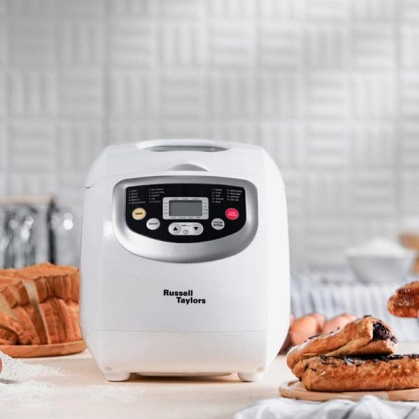 Russell Taylors BM-10 white bread maker with digital display on kitchen counter, surrounded by fresh baked bread loaves and slices.