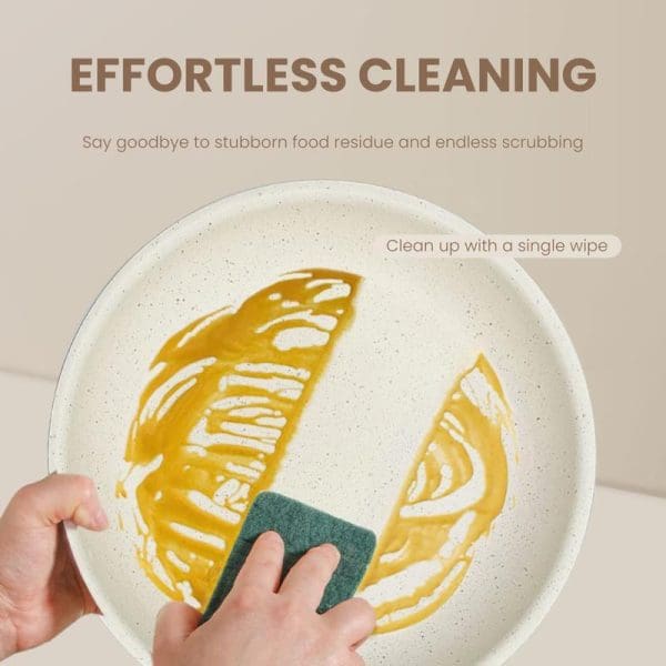 Hand cleaning a white speckled non-stick frying pan with green sponge, removing yellow food residue easily with single wipe, demonstrating effortless cleaning feature.