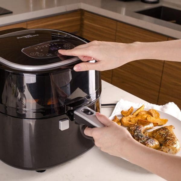 Russell Taylors Digital Rotary Air Fryer AF-76 7.5L with hands operating touch controls and removing cooked chicken and potato wedges from drawer basket.