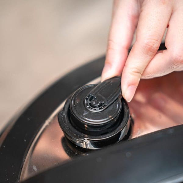 Hand pressing button on black Russell Taylors Electric Pressure Cooker PC-12 12L Multi Rice Cooker with non-stick pot control panel.