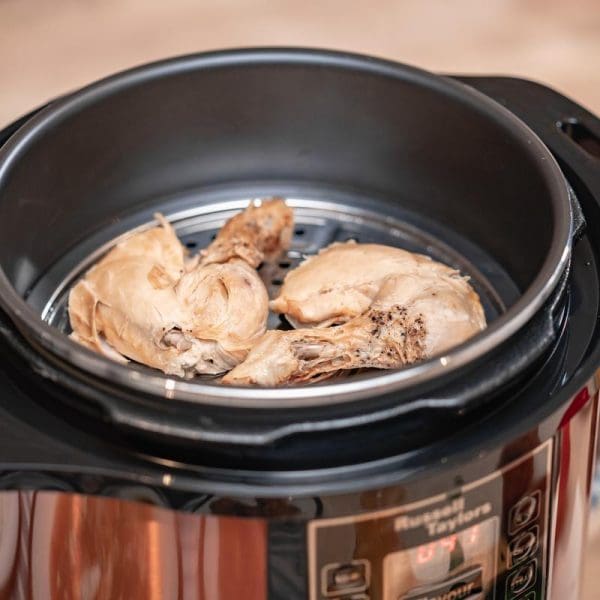 Russell Taylors 12L Electric Pressure Cooker PC-12 with non-stick pot containing cooked chicken pieces on steaming rack, copper-colored exterior with digital controls.