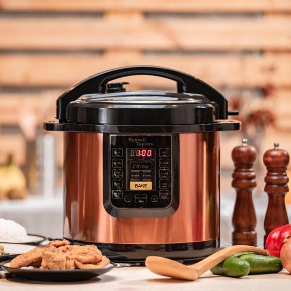 Russell Taylors 8L stainless steel electric pressure cooker with copper finish, digital display, and black handle on kitchen counter with vegetables and spices.