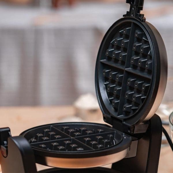 Russell Taylors Rotating Waffle Maker WM-30 with open lid showing non-stick waffle plates and grid pattern, displayed on kitchen counter with blurred background.
