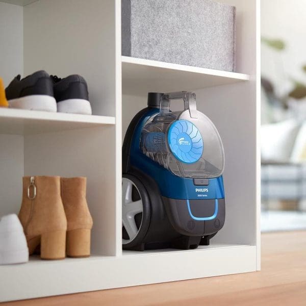 Philips FC9352 PowerPro Compact Bagless Vacuum Cleaner berwarna biru dan hitam diletakkan di dalam rak putih bersama kasut dan stor barang rumah